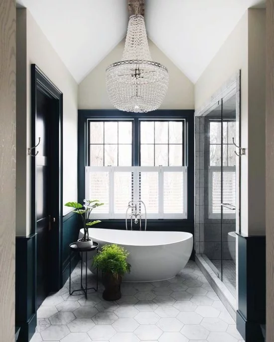 Pariser Chic im Bad moderne Badewanne ovale Form schickes Raumdesign zwei Grünpflanzen als Akzent großes Fenster Kristall-Kronleuchter