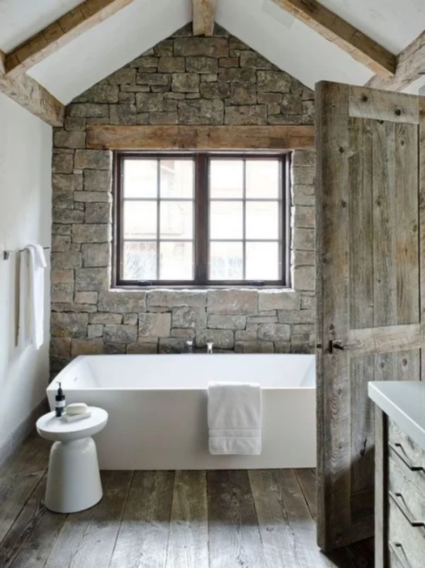 Stein im Bad rustikaler Stil Steinwand rechteckiges Fenster Holztür moderne Badewanne Hocker Tuchhalter