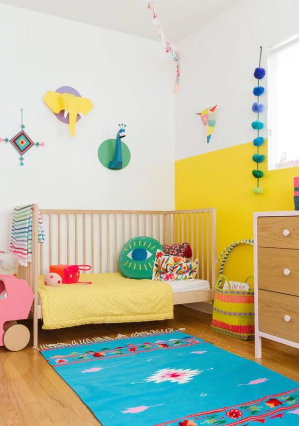 Kunterbuntes Babyzimmer blauer Teppich gelbe Wand Raumdekoration Bett bunte Kissen Babyspielsachen