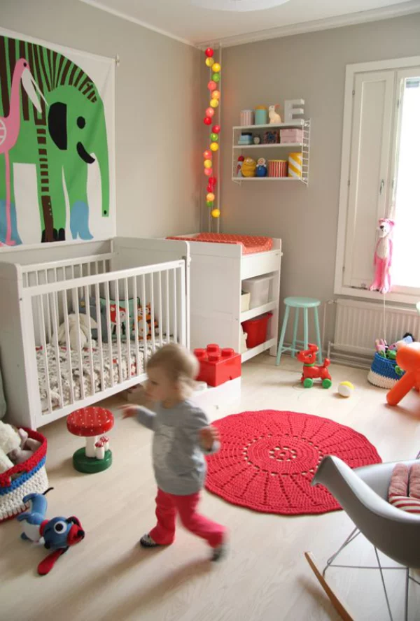 Kunterbuntes Babyzimmer roter runder Teppich gestrickt Baby spielt Wanddekoration