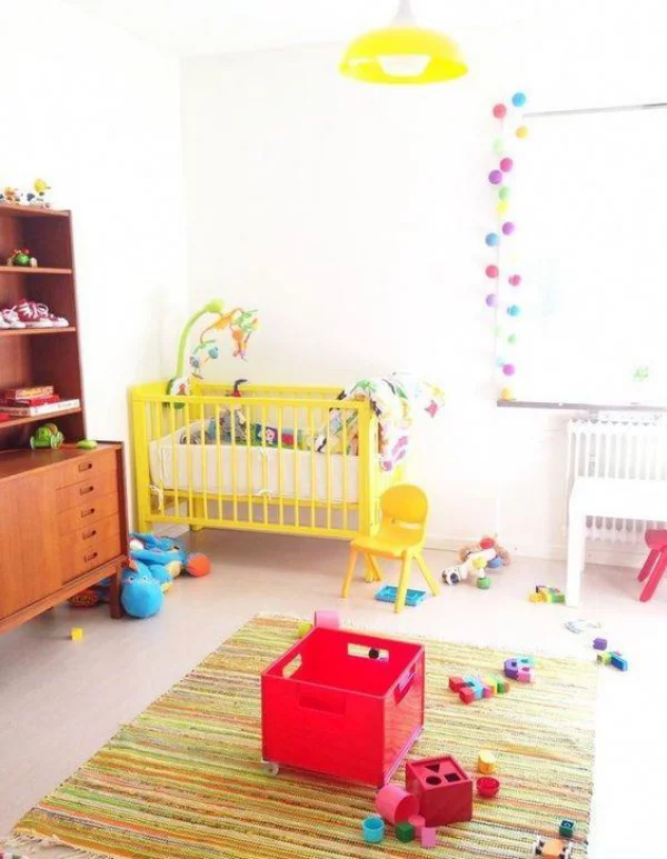 Kunterbuntes Babyzimmer viele Spielsachen Teppich Girlanden am Fenster gelbes Bett